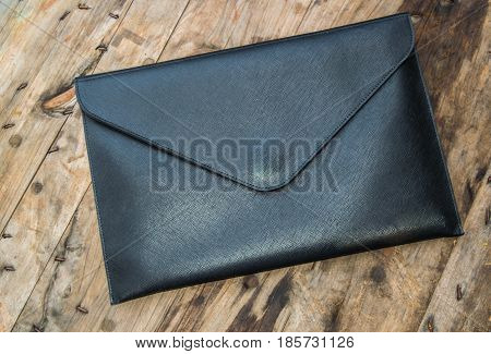 Black leather business bag placed on a wooden floor.