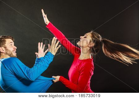 Wife abusing husband. Aggresive woman beating slapping scared man. Couple in studio on black. Domestic violence aggression. Bad relationship.