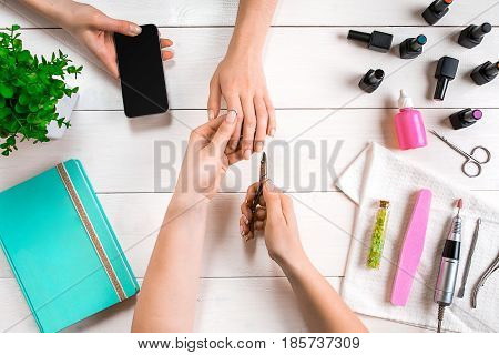 Manicure for the client. Close-up of the hands of a manicurist and client on a wooden background. Nail care. Manicure set and nail polish.