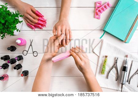 Manicure for the client. Close-up of the hands of a manicurist and client on a wooden background. Nail care. Manicure set and nail polish.