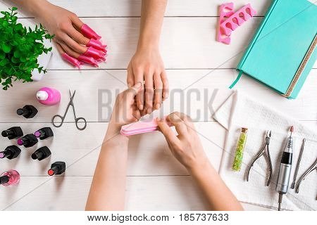 Manicure for the client. Close-up of the hands of a manicurist and client on a wooden background. Nail care. Manicure set and nail polish.
