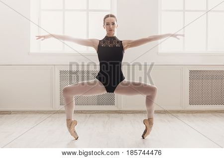 Graceful ballerina practice ballet plie position near large window in light hall. Ballet class training, high-key soft toning, copy space