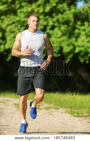 Runner - running athlete man. Male sprinting during outdoors training for marathon run. Athletic fit young sport fitness model in his twenties in full body length on road outside in nature