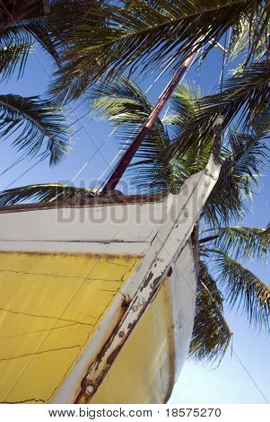Uno sloop a scafo giallo si siede su una spiaggia tropicale.