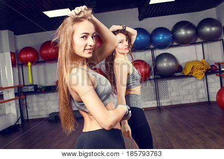 Two athletic girls training in fitness center. Smiling fitness women dancing exercises in gym