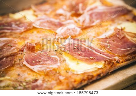Detail of rustic ham and brie cheese pizza sprinkled with provencal herbs
