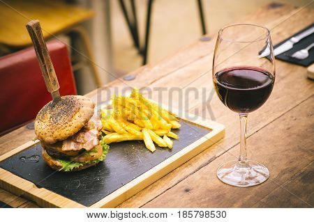 Traditional chips and buger with glass of red wine on rustic table