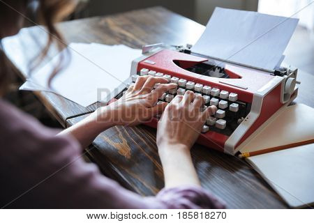 Close up portrait of an authoress sitting at the table and typing on typerwriter indoors
