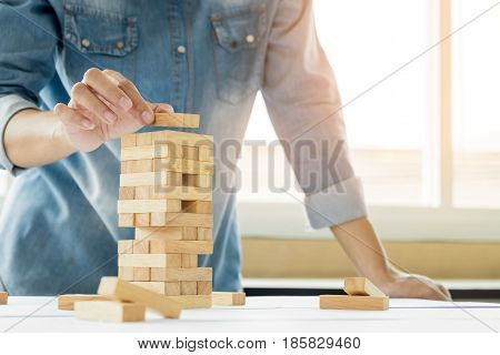 Hand Of Engineer Playing A Blocks Wood Tower Game (jenga) On Blueprint Or Architectural Project.