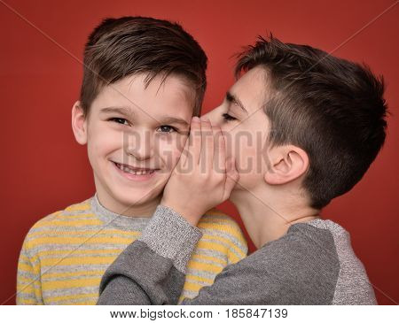 Young boy whispering secret into ears of smiling brother