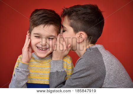 Young boy whispering secret into ears of smiling brother