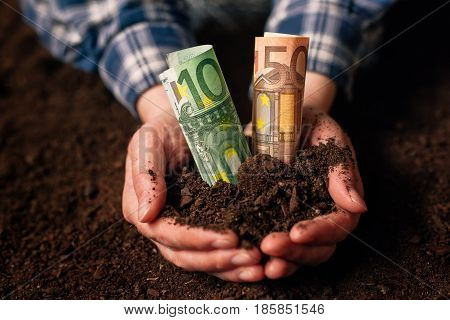 Hands with fertile soil and euro money banknotes female farmer handful of cultivated land that makes profit and steady income from sustainable agricultural activity like organic growth of crops