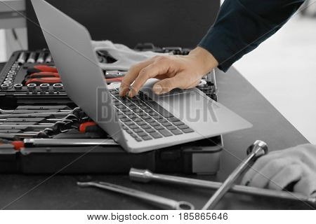 Auto mechanic working with laptop in car repair shop, closeup
