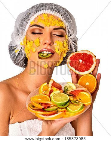 Facial mask from fresh fruits for woman. Girl in medical hat give slices of avocado, grapefruit and kiwi as ingradients for face care smooth skin on isolated. Girl is eating a piece of kiwi.