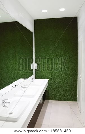Three white sinks in empty toilet with big mirror and green lawn wall