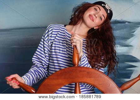 The girl in the pirate hat wearing marine vest holds the helm of the ship and smiling