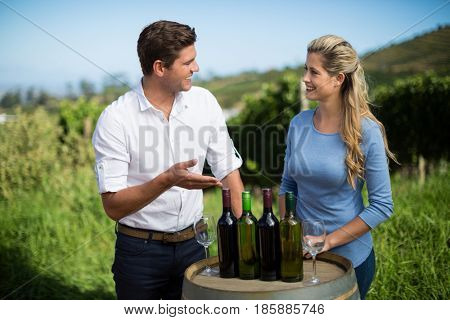 Smiling friends standing by wine bottles on berrel at vineyard