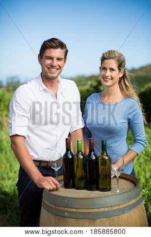 Portrait of happy friends standing by wine bottles on berrel against clear blue sky at vineyard