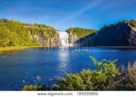 Sunny autumn day. The vast blue lake and powerful waterfall Montmorency in Montmorency Falls Park, in vicinities Quebec. The concept of active and cultural tourism