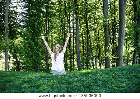 A girl is sitting looking at the forest and is happy. Rear view.