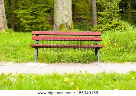 Empty dark red wooden bench in the park. A place to sit in nature. Natural bench beside the park.