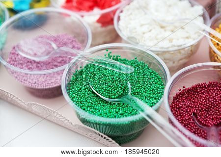 Ice cream treats and toppings sale. Rainbow sprinkles, stars, non pareil and glitter cupcake decorations, bright green. Closeup in plastic plates with spoons. Confectionery store