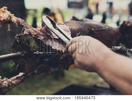 Barbecue picnic at country fair. Lamb roasted at spit. Grill, big piece of meat at rolling skewer. Street vendor, professional chef hands cooking bbq food, unrecognizable. Catering concept