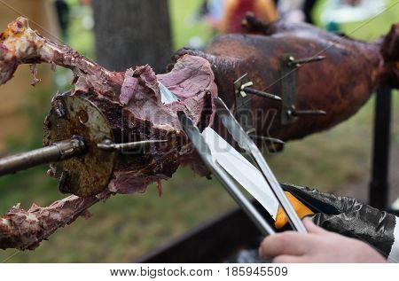 Barbecue picnic at country fair. Lamb roasted at spit. Grill, big piece of meat at rolling skewer. Street vendor, professional chef hands cooking bbq food, unrecognizable. Catering concept
