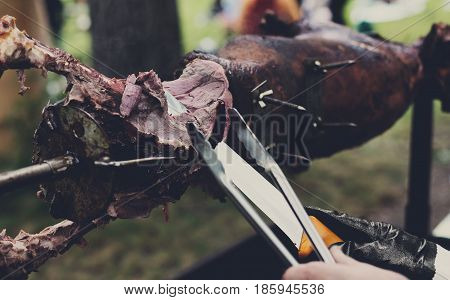 Barbecue picnic at country fair. Lamb roasted at spit. Grill, big piece of meat at rolling skewer. Street vendor, professional chef hands cooking bbq food, unrecognizable. Catering concept