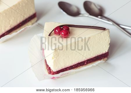 Cheesecake with red currant and chocolate strip serving slices and teaspoons on background. Tasty dessert with berries.