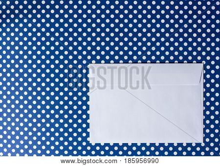 White paper envelope on a blue background polka dot. View from above.