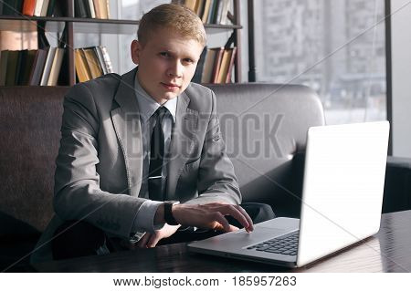 elegant businessman sitting at desk with laptop. looking at the camera. the hand is on the laptop and moving fingers on the trackpad