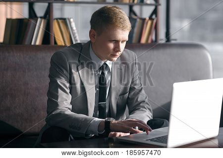 young businessman sitting at desk and working with laptop. looks at the laptop and moving fingers on the trackpad