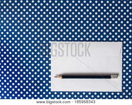 White paper envelope and black pencil on a blue background polka dot. Top View.