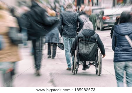 Disabled man sitting in a wheelchair on a budy street among crowd of people