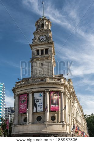 Auckland New Zealand - March 5 2017: The white stone Clock Tower of town hall with theater posters and flag. Blue sky with white clouds.