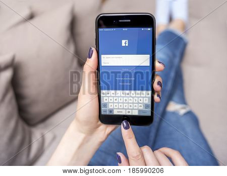UZHGOROD, UKRAINE - MAY 11, 2017: New black iPhone 7 Plus, with social network Facebook in the hands of the woman sitting on the couch, on May 11, 2017 in Uzhgorod, Ukraine.