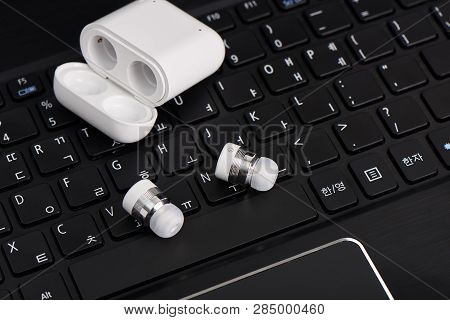 Wireless Cordless Bluetooth Earbuds With Chargeable Case On A Keyboard Of Laptop Computer