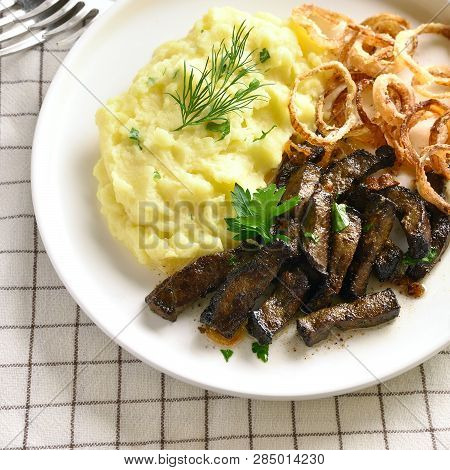 Close Up Of Roasted Beef Liver With Mashed Potatoes And Fried Onion Rings On White Plate. Pieces Liv