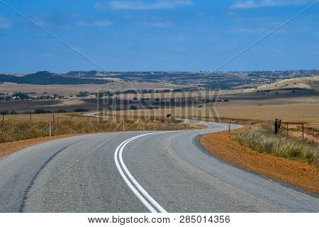 Australian Bush Road Curving Through Dry Landscape With Yellow Farmland