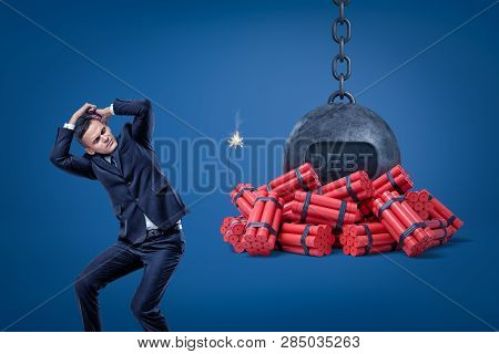Businessman Protecting Himself With Hands And Chained Ball With A Debt Sign Over Red Dynamite Sticks