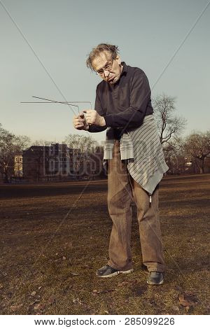 Man In Ugly Style Dress Practicing In Dowsing With Rods