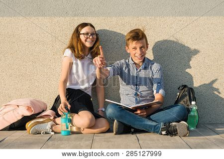 School Children Teens Sit On Gray Wall, Read Textbooks, Drink Water, Look At Textbook. Boy Looking A