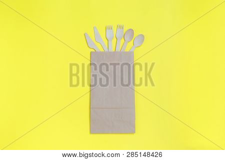 Disposable Tableware From Natural Materials, Wooden Spoons, Knives, And Forks In Paper Bag On Yellow