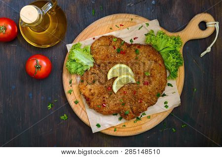 Large Viennese Schnitzel On A Wooden Board With Lemon On A Dark Background. Meat Dish. Top View, Fla