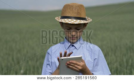 Farmer Boy In A Hat Uses A Tablet In The Field, Checks The Crop