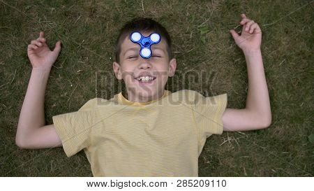 Happy Boy Twists The Spinner On Nose And Lies On Grass Outdoors