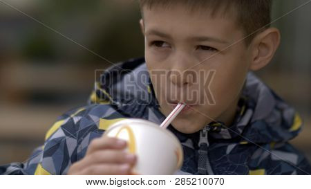 Boy Drinks A Milkshake At A Cafe Outdoors