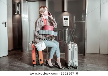 Busy Wife Sitting On Suitcase And Calling Her Husband While Waiting