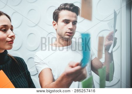 Portrait Of Two Coworker People Standing At Office Space Behind Glass Wall With Sticky Notes. Team O
